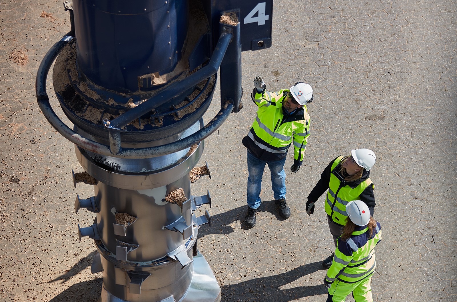 three workers looking up and pointing at screw conveyor